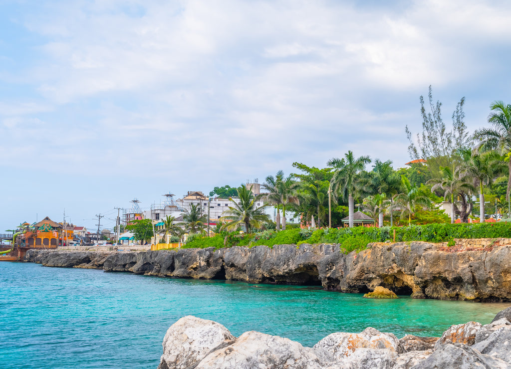 Beautiful coastal cliffside turquoise ocean on Caribbean island. Sunny summer vacation day on the coast of Montego Bay, Jamaica. Ideal tropical tourist destination. Margaritaville in background