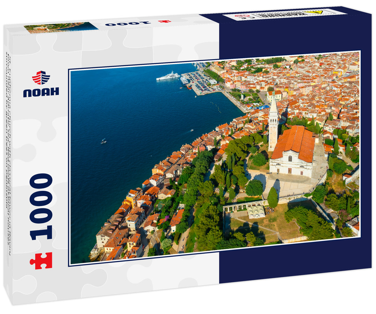 St. Euphemia church with classical tower in Rovinj town near Adriatic sea. Red roofs of local houses surrounded by green trees on peninsula