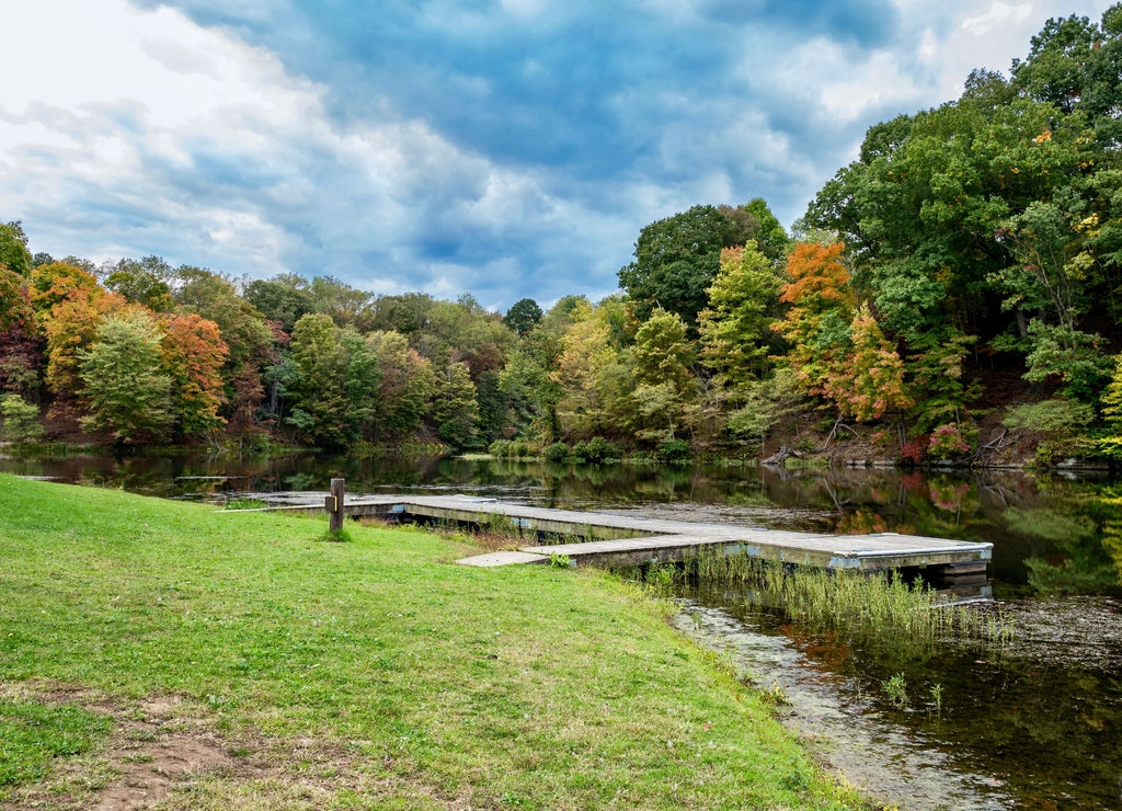 Tomlinson Run State Park in the fall in West Virginia with the fall colors and trees reflecting in the lake, the blue cloud filled sky in the background and a tranquil serene nature landscape scene