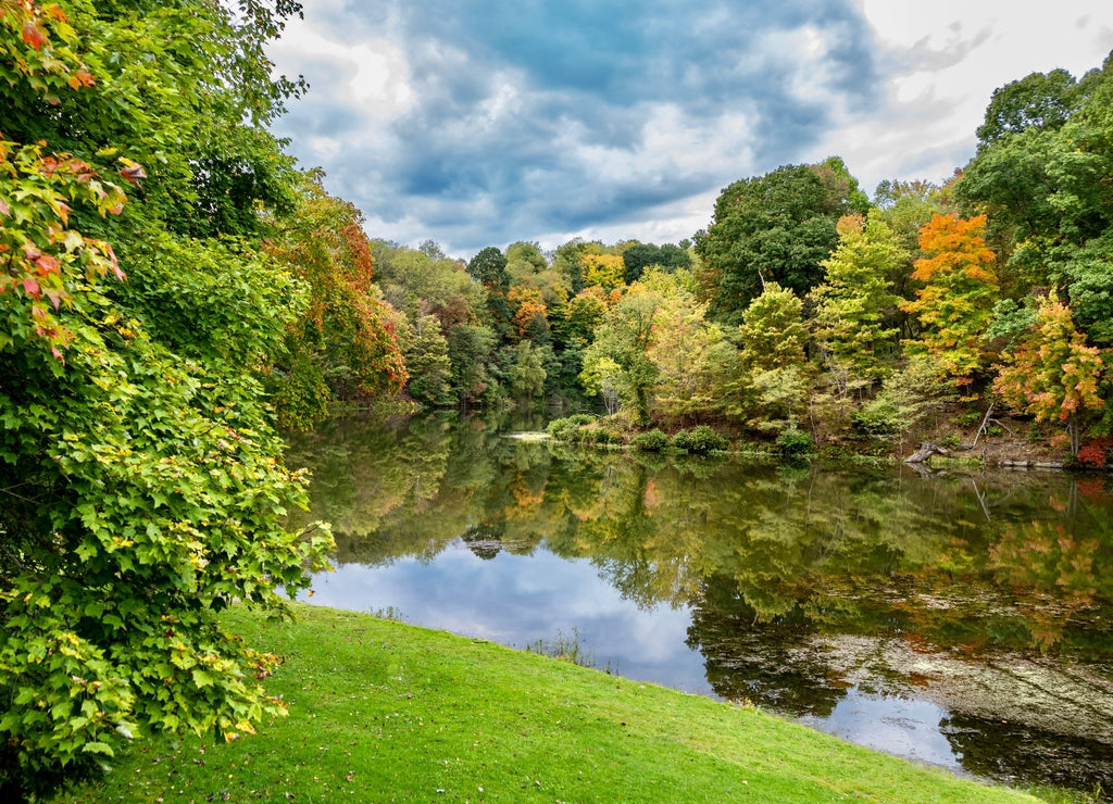 Tomlinson Run State Park in the fall in West Virginia with the fall colors and trees reflecting in the lake, the blue cloud filled sky in the background and a tranquil serene nature landscape scene