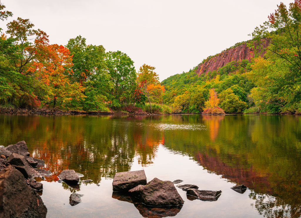 Beautiful fall woodland with rocks and reflections in the river water. Tranquil autumn forest image with space for texts and design. Mill River landscape at East Rock Park in New Haven, Connecticut