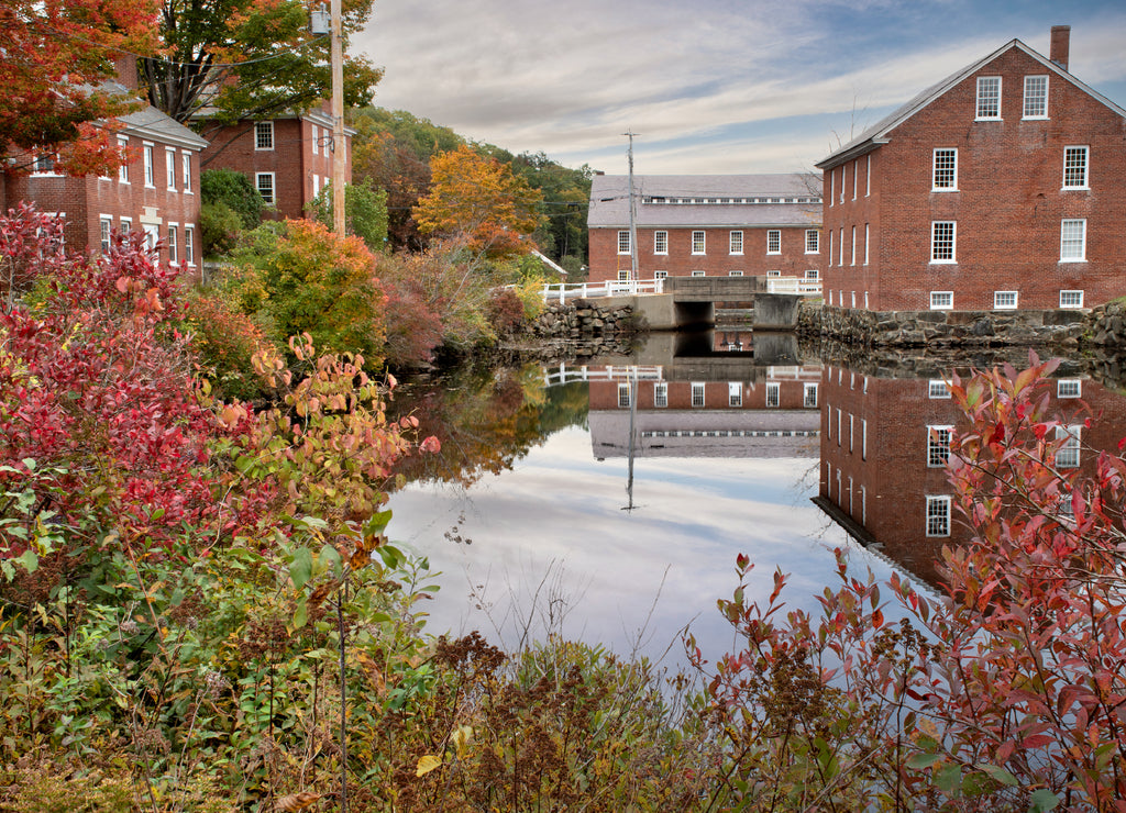 Colorful autumn scene at historic 19th-century textile mill town in Monadnock region of New Hampshire. Picturesque village of Harrisville with reflection of sky and red brick buildings on water