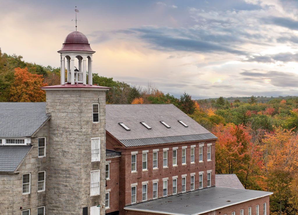 Beautiful sky and colorful autumn scene in historic town of Harrisville, New Hampshire. Old bell tower and preserved textile mill buildings built of granite and brick in 19th century