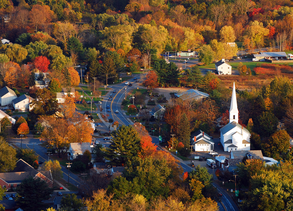 A classic New England town, with a white church with a large steeple, is surrounded by brilliant autumn foliage in an aerial view, New Hampshire