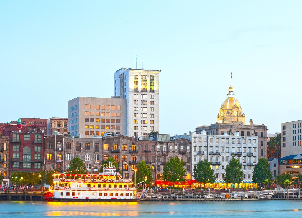 Savannah Georgia USA, skyline of historic downtown at sunset with illuminated buildings and steam boats