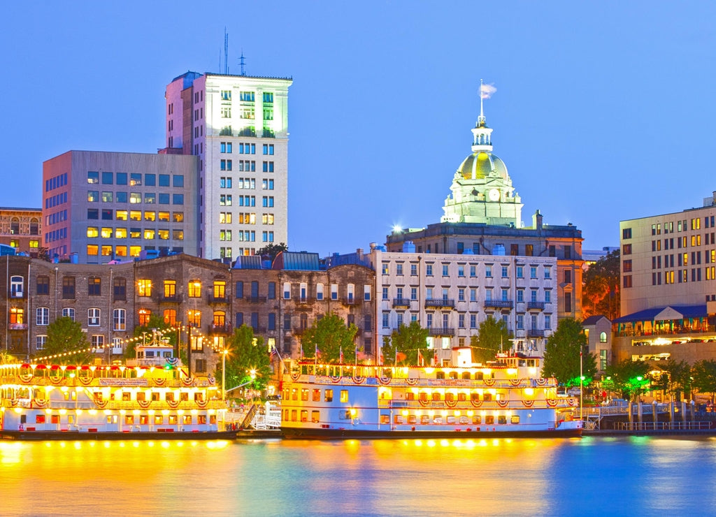 Savannah Georgia USA, skyline of historic downtown at sunset with illuminated buildings and steam boats