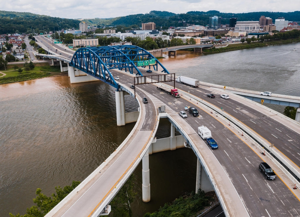 This is an aerial of a blue, eight-lane highway arch bridge that carries Interstate 64 over the Kanawha River in Charleston, West Virginia