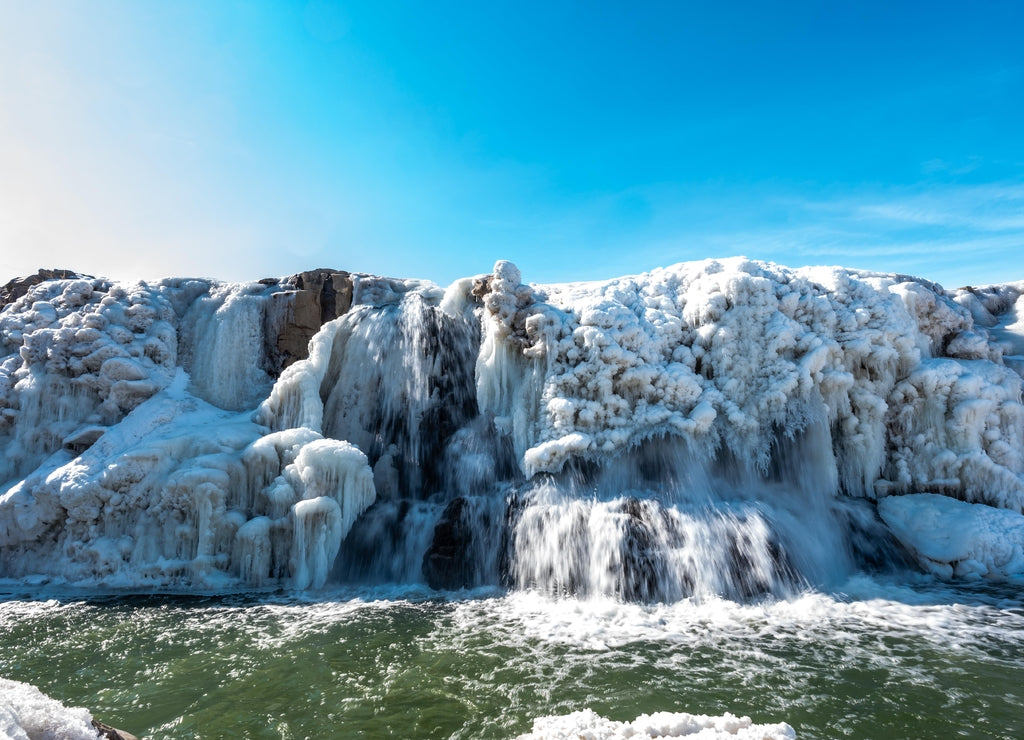 Sioux Falls Park waterfall with ice and snow. Cascading snowmelt water pouring over the top into a pool of standing water