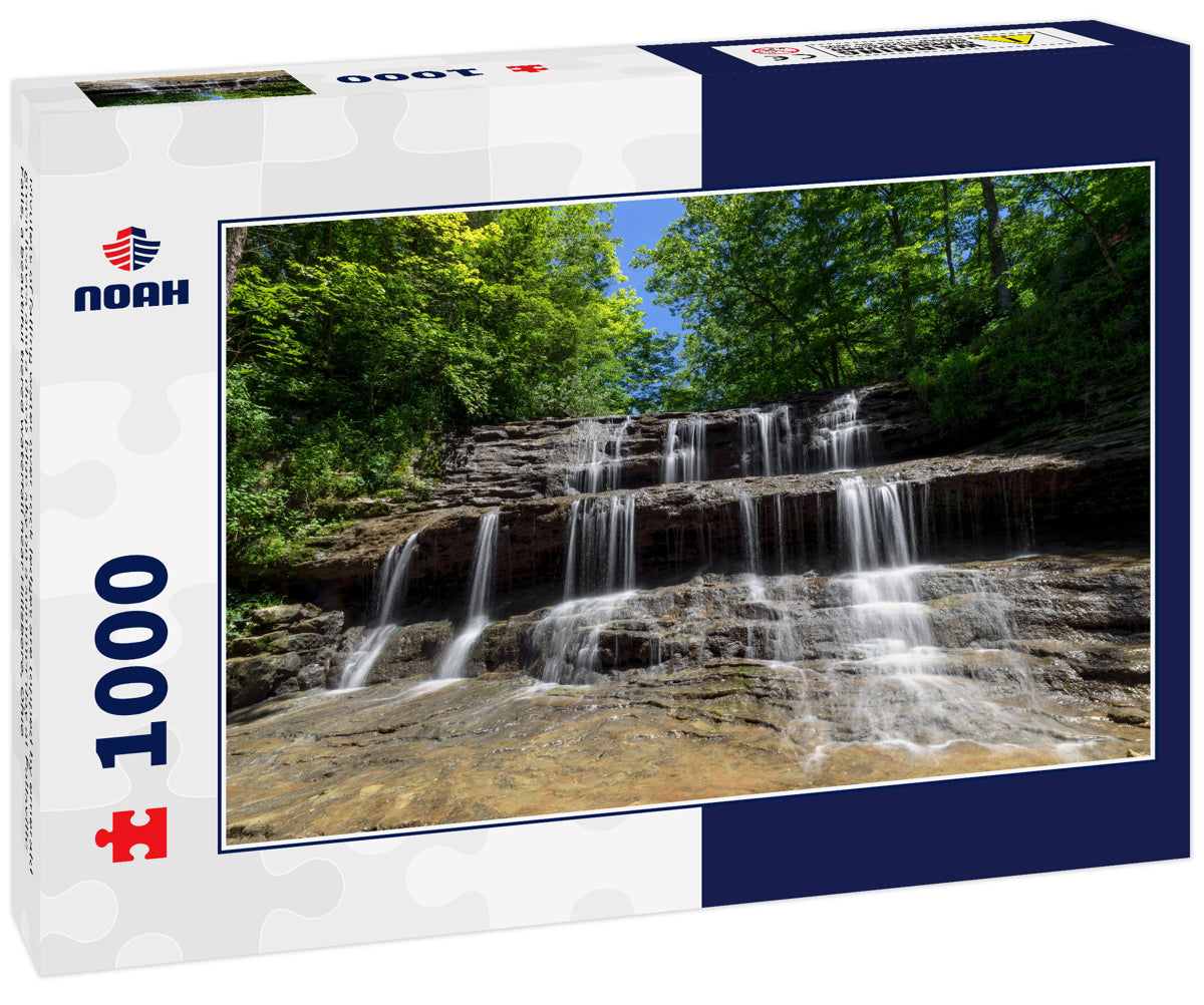 Rivulets of falling water over rock ledges are topped by emerald green leaves and a deep blue sky on a summer day at Fallsville Falls, a beautiful tiered waterfall near Hillsboro, Ohio