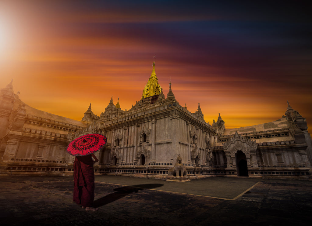 Asian young monk holding red umbrella on the Ananda temple at sunset in Bagan, Myanmar