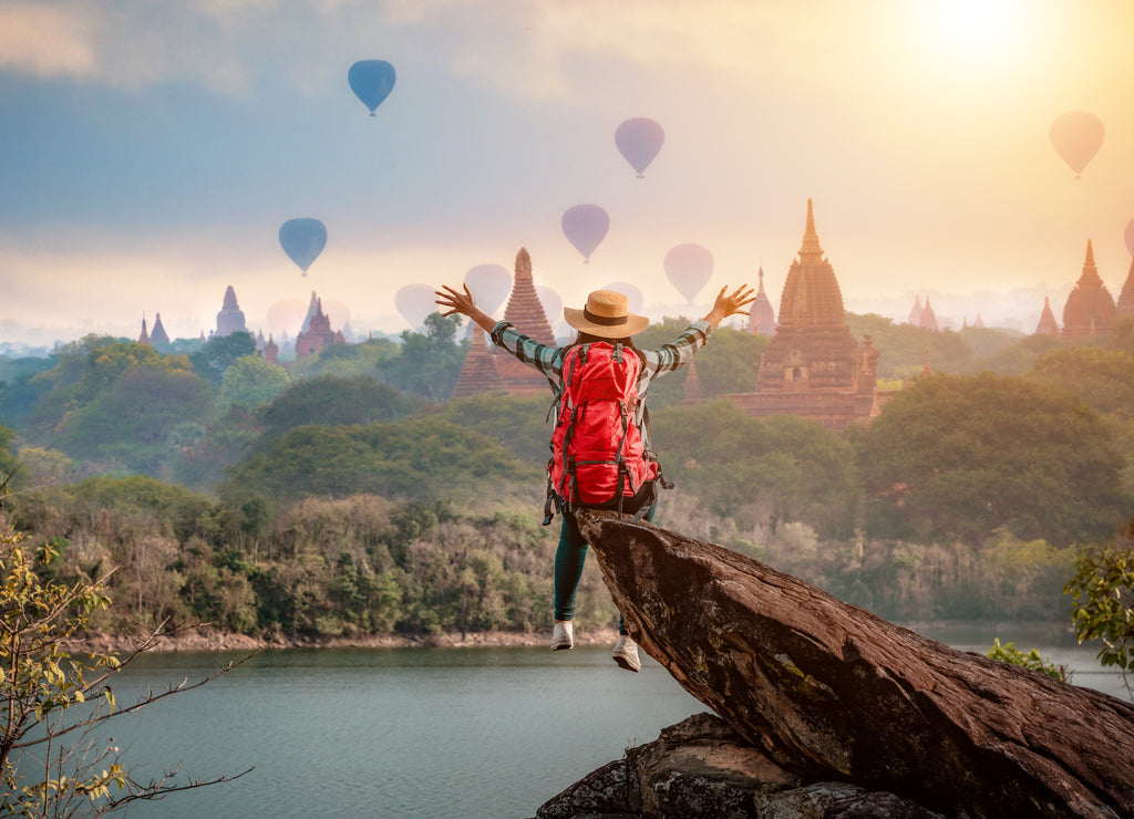 Woman traveler sitting on stone freedom hands up watching and enjoying with Bagan pagoda landscape in Mandalay Myanmar