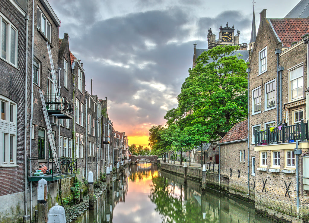 A canal in the old medieval town centre of Dordrecht, the Netherlands, with houses on both sides and an orange red sunset in the distance