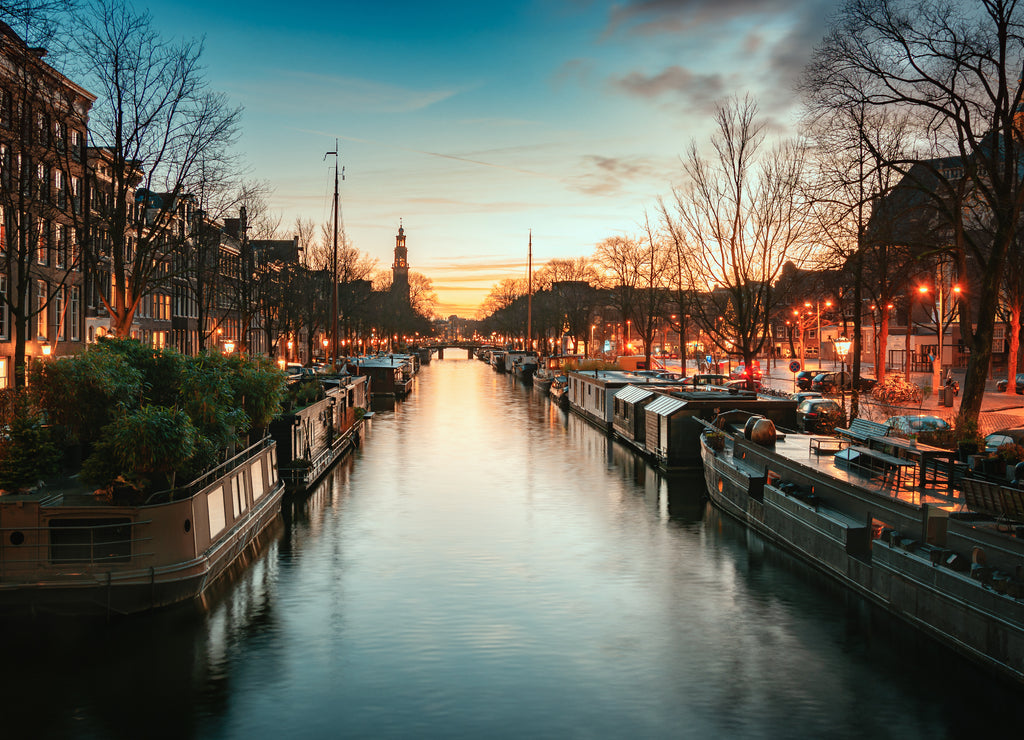 Houseboats in the Prinsengracht in the old center of Amsterdam with the spire of the Westertoren in the background during sunset
