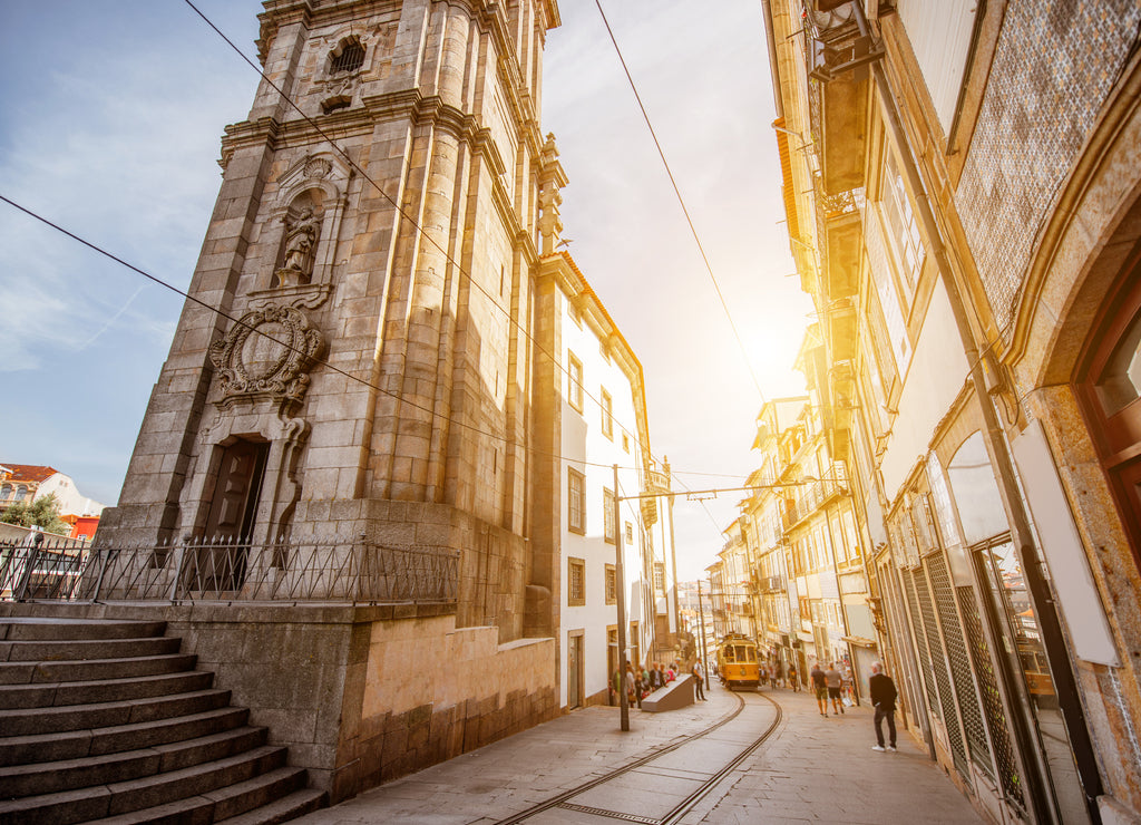 Street view with Clerics church tower with retro tram during the sunrise in Porto city, Portugal