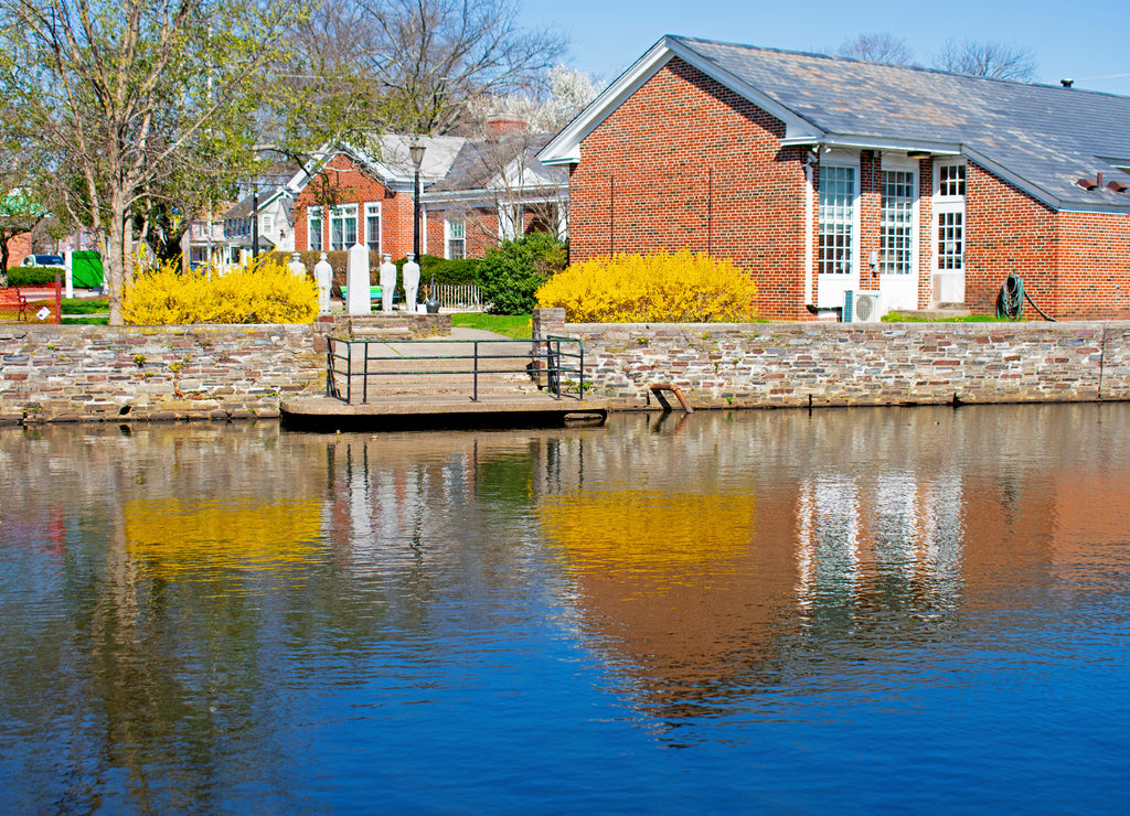 Reflections of buildings, trees, and flowering bushes in the waters of Peddie Lake in East Windsor, New Jersey, on a bright and sunny day -03