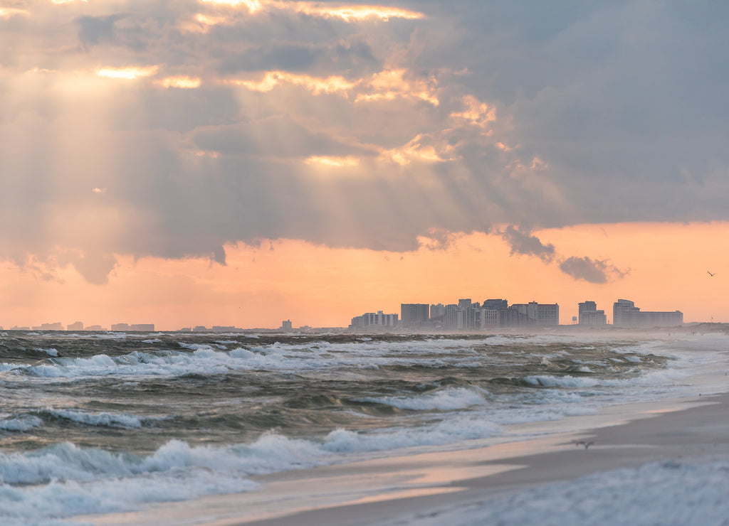 Dramatic magical pastel light sunset with sun rays in Santa Rosa Beach, Florida with Pensacola coastline coast cityscape skyline in panhandle and ocean gulf mexico waves