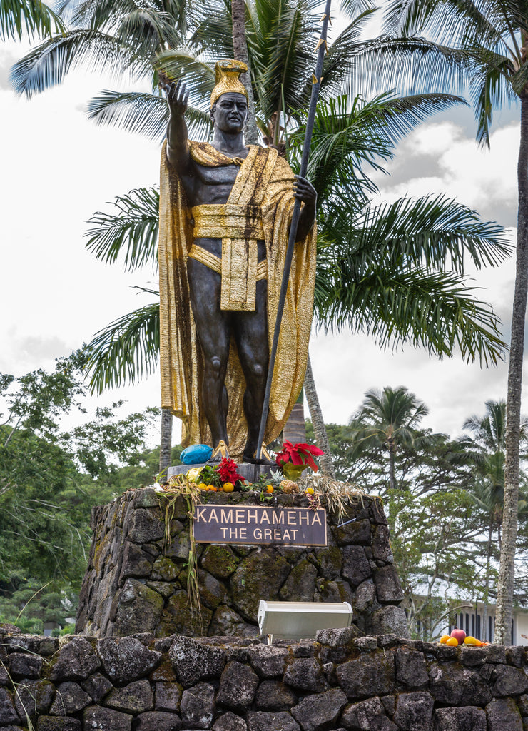 Hilo, Hawaii, USA: Closeup of statue of King Kamehameha, decorated with golden attore amdcrown and long spear under white cloudscape and green trees as backdrop