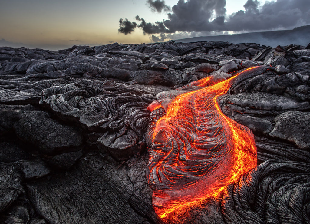 Red Orange vibrant Molten Lava flowing onto grey lavafield and glossy rocky land near hawaiian volcano with vog on background, Hawaii