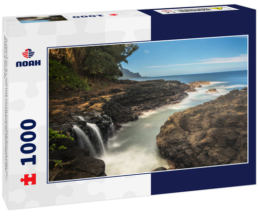 Rugged rocks around small waterfall falling into the ocean with the Na Pali coastline by Hanalei in the distance Hawaii