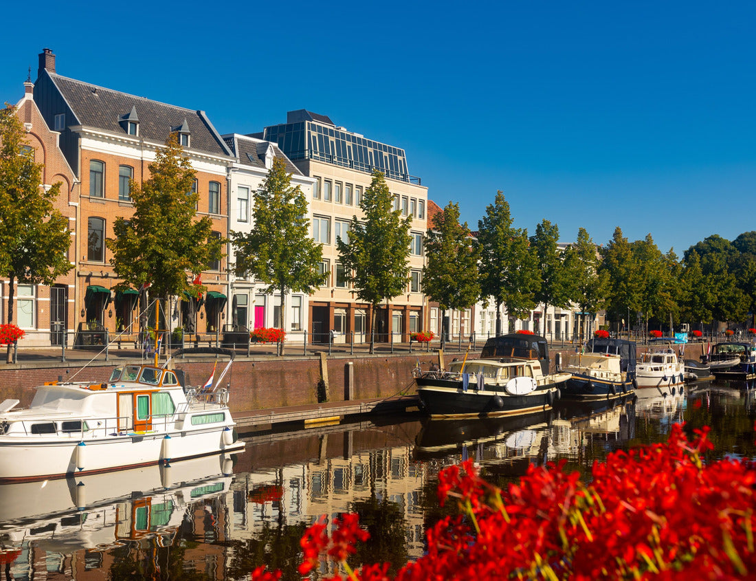 Noah Jigsaw Puzzle Mark River dam in Breda, Netherlands. View of red flowers in bloom, buildings and boats along the river banks 1000 pieces