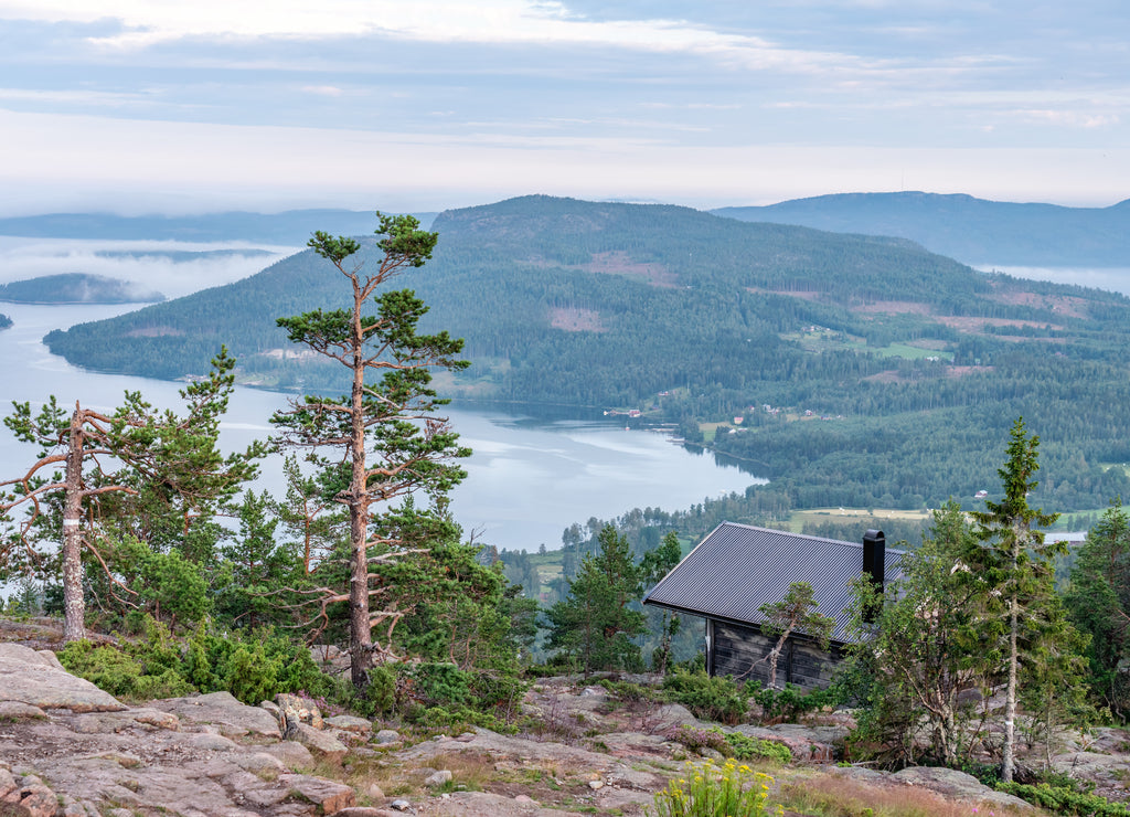 Public tourist rest house in front of view over Scandinavian mountains with pine tree forest, the village and two sea bays, summer day with heavy dramatic clouds, North Sweden