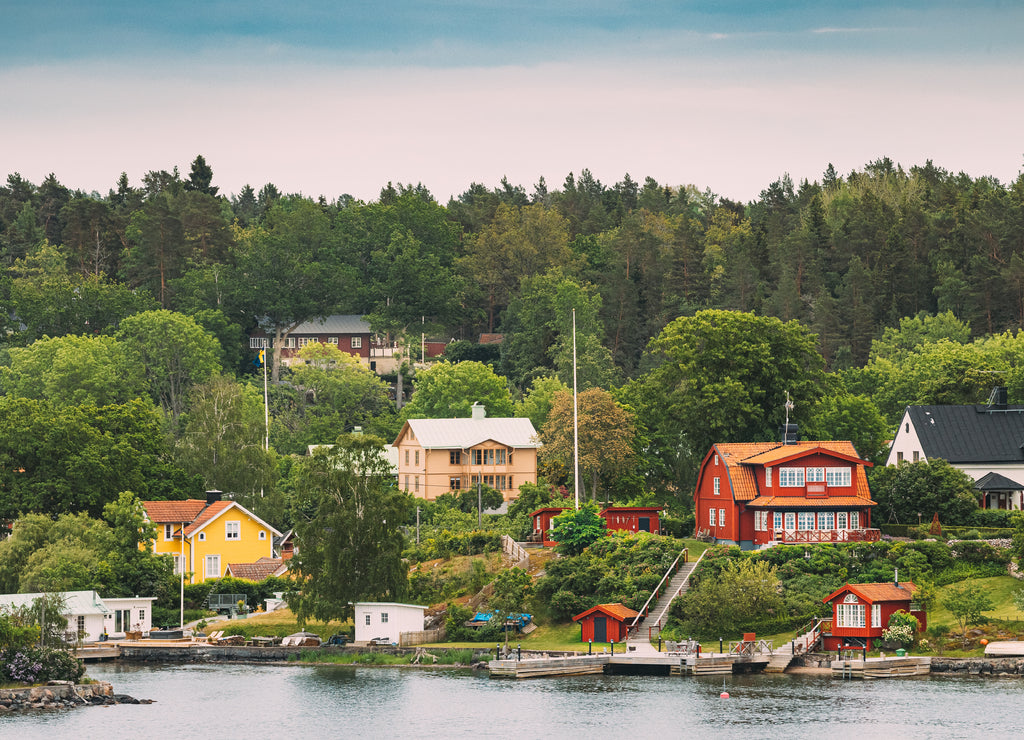 Sweden. Beautiful Red And Yellow Swedish Wooden Log Cabins Houses On Rocky Island Coast In Summer Evening