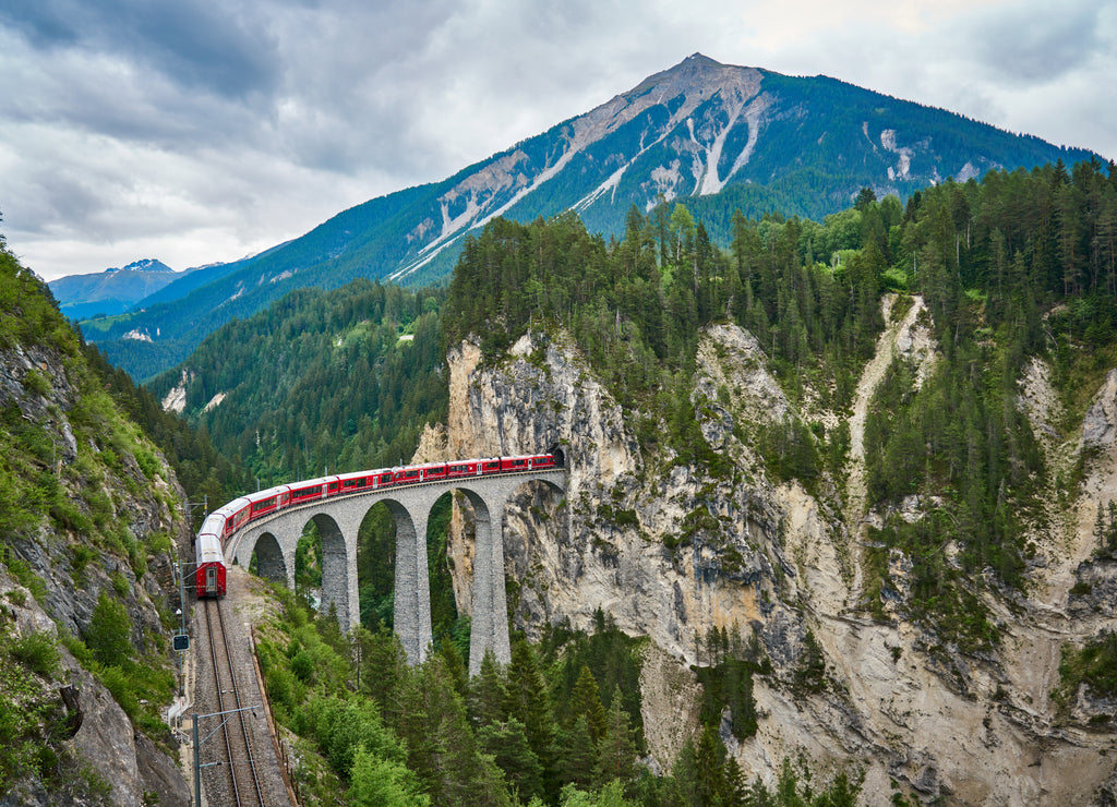 Red train passes above the Landwasser Viaduct bridge, in canton of Graubünden, Switzerland. Bernina Express / Glacier Express uses this railroad