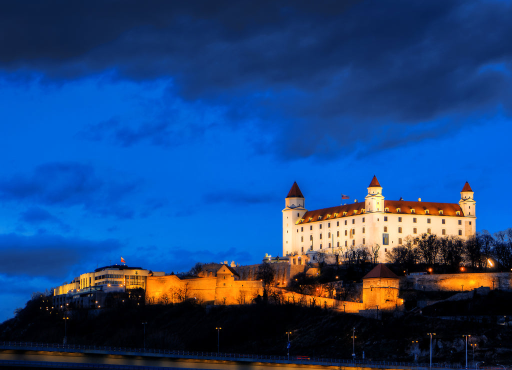 Night view of Bratislava castle from river surface with dramtic sunset skyline, Slovakia