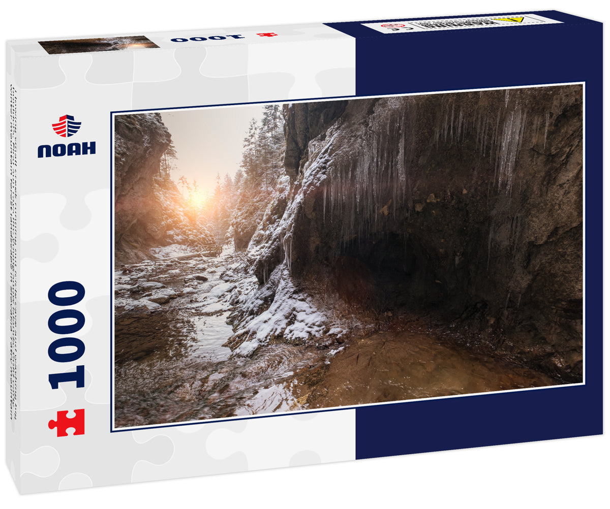 Flowing small creek running out icicle cave and washing big boulders. First sun rays lite young snow islands. Cold early winter mountain forest landscape in Slovakia Tatry mountain