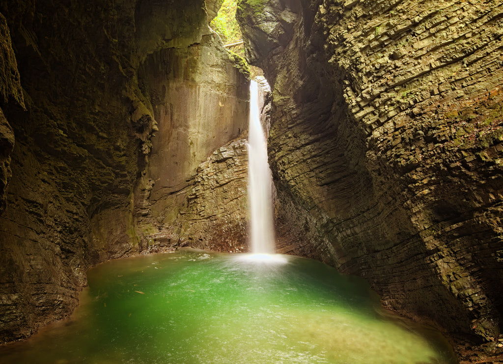 Mystical view of the rocky amphitheatre with a green pool and a white beam of water. 15-metre-high Kozjak Waterfall (Slap Kozjak). Protected natural treasure. National Park of Triglav, Slovenia