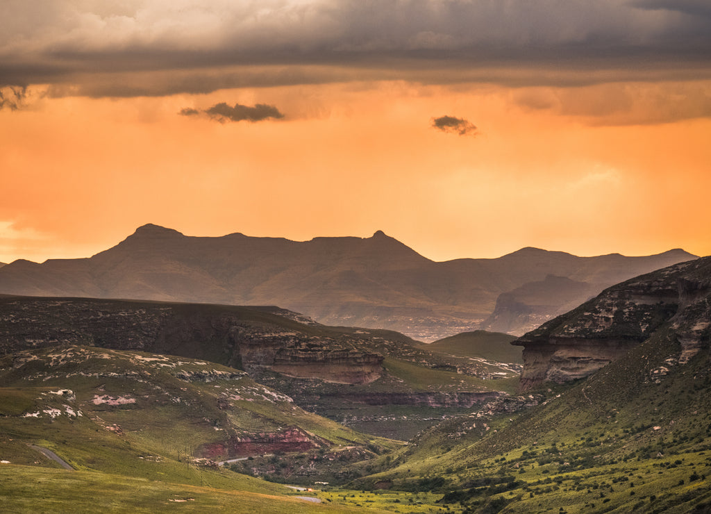 A dramatic scene of golden sunset and storm clouds over the Drakensberg mountains surrounding the Amphitheatre, seen from Golden Gate Highlands National Park in the Drakensberg, South Africa