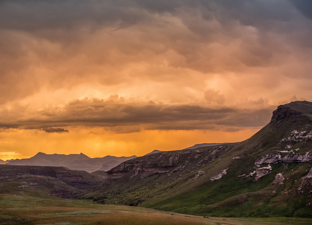 Cliffs and mountains under dramatic colorful storm clouds at sunset over the Drakensberg mountains surrounding the Amphitheatre, seen from Golden Gate Highlands National Park, South Africa