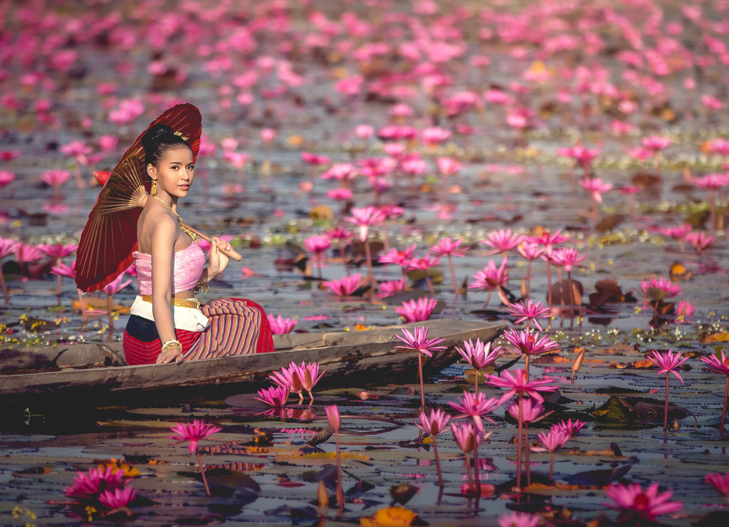 Asia women on the boat in the lotus pond. She wears Thai traditional dresses