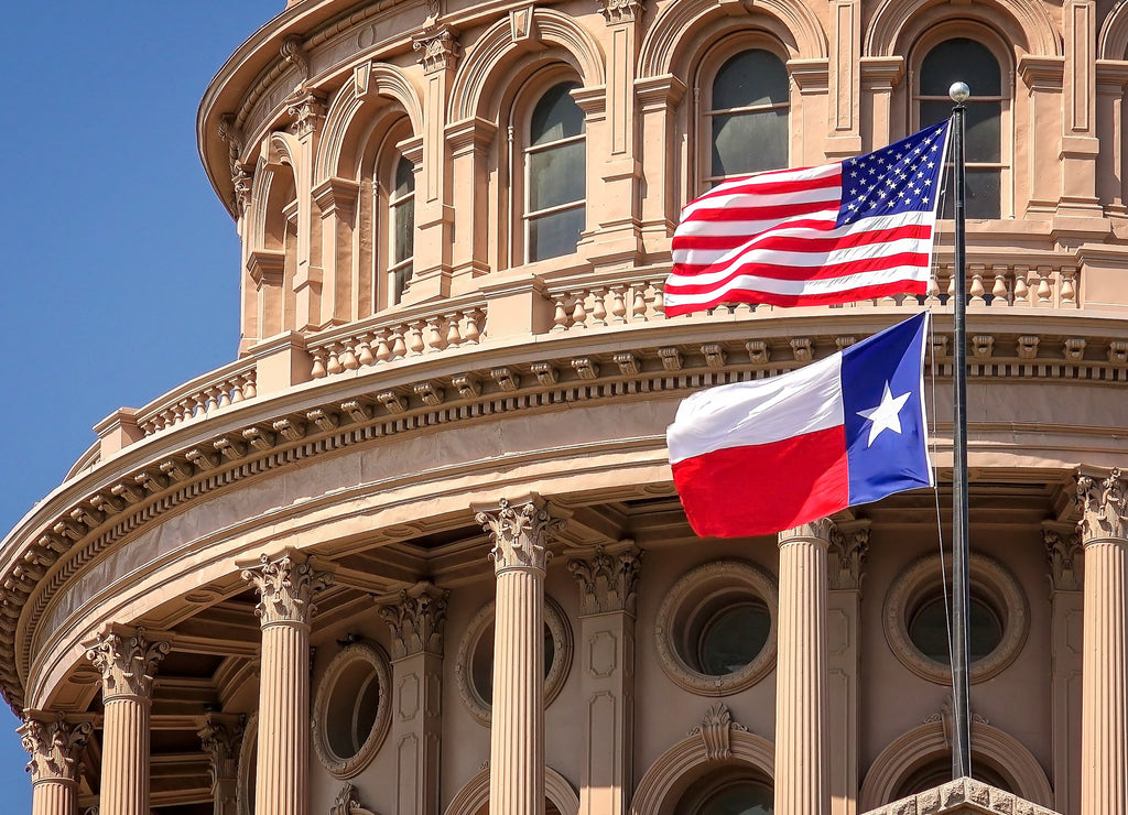 American and Texas state flags flying on the dome of the Texas State Capitol building in Austin