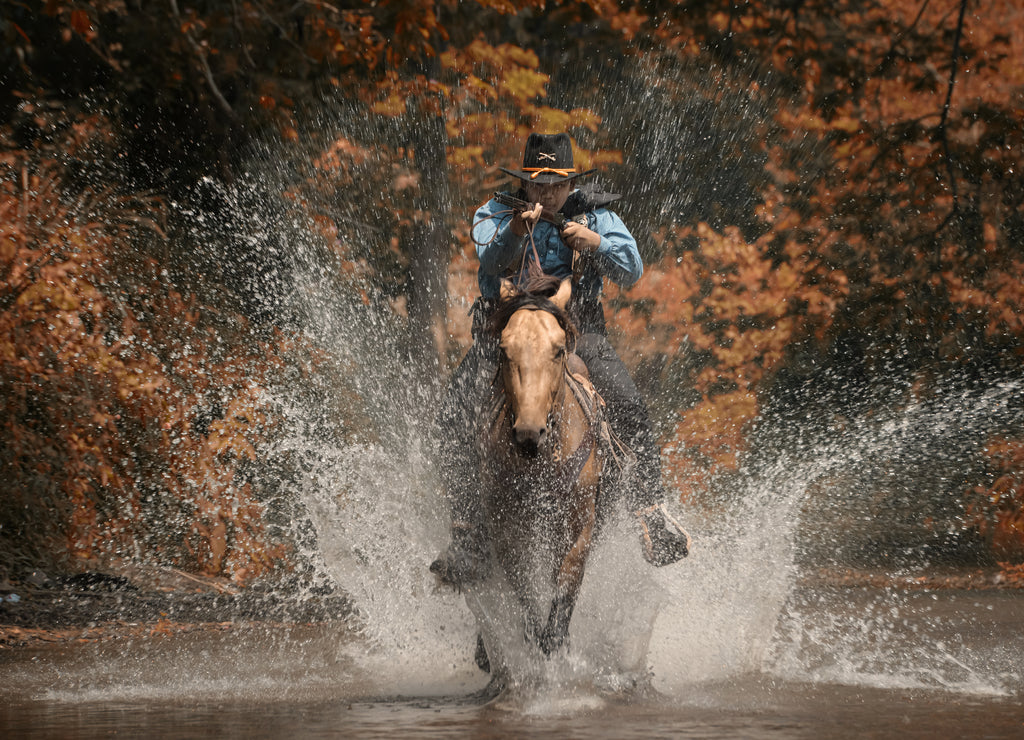 A vintage action shot of a cowboy riding a horse, wading through the water and holding a rifle, Texas