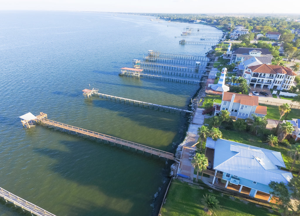 Aerial view three-story waterfront vacation home with fishing piers stretching out over the Galveston Bay in Kemah city, Texas, USA. Bird eye view of Kemah Lighthouse District at sunset