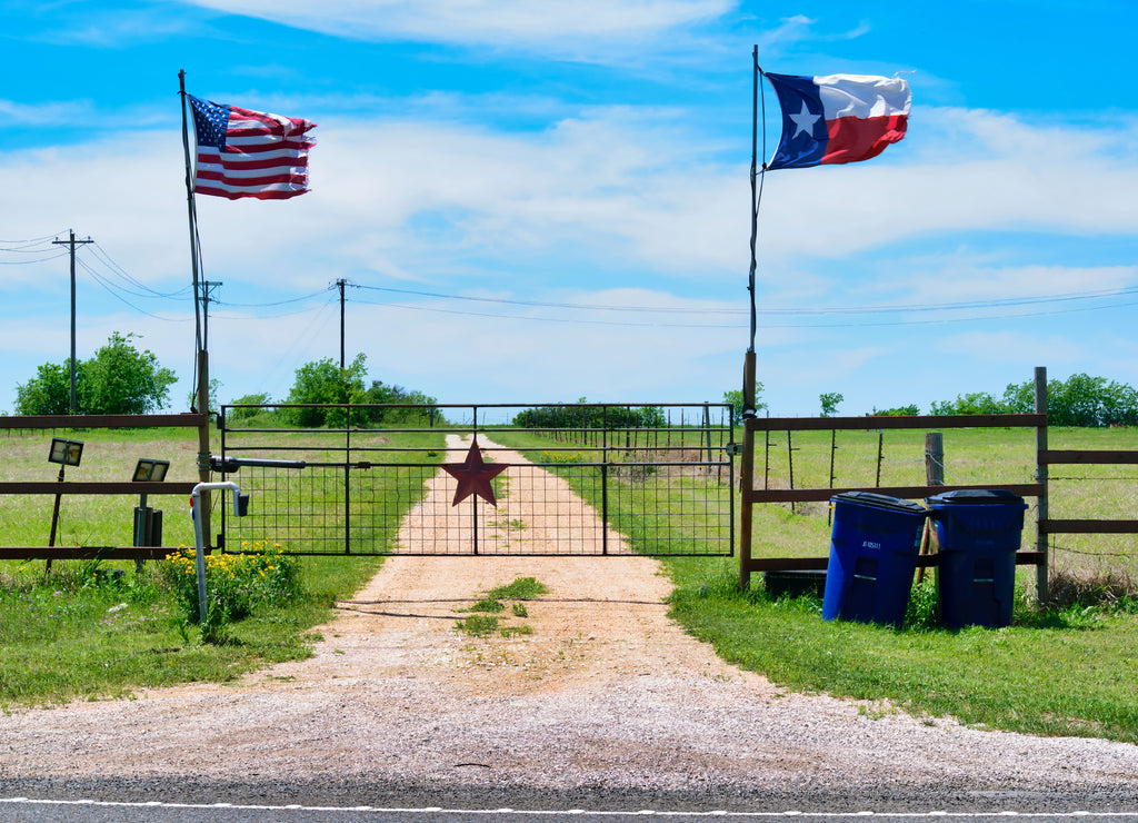 American and Texas state flags flying near countryside gate, Texas rustic star with road to the house slowly dissolving in the background