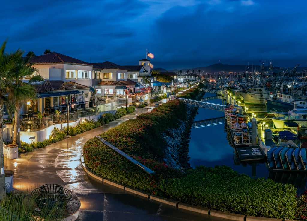 Ventura Harbor Village boardwalk is reflective and wet from the early morning rain with rain clouds reflected in harbor water California