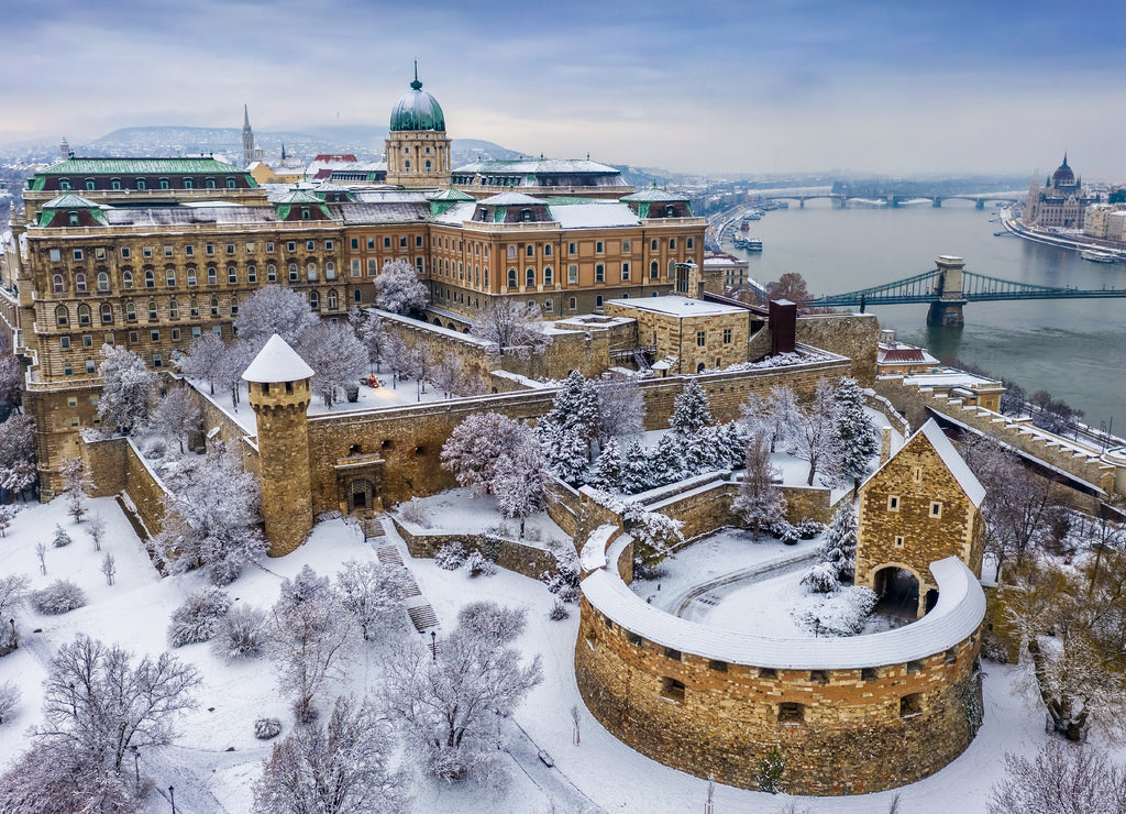 Budapest, Hungary - Aerial view of the snowy Buda Castle Royal Palace from above with the Szechenyi Chain Bridge and Parliament of Hungary at winter time