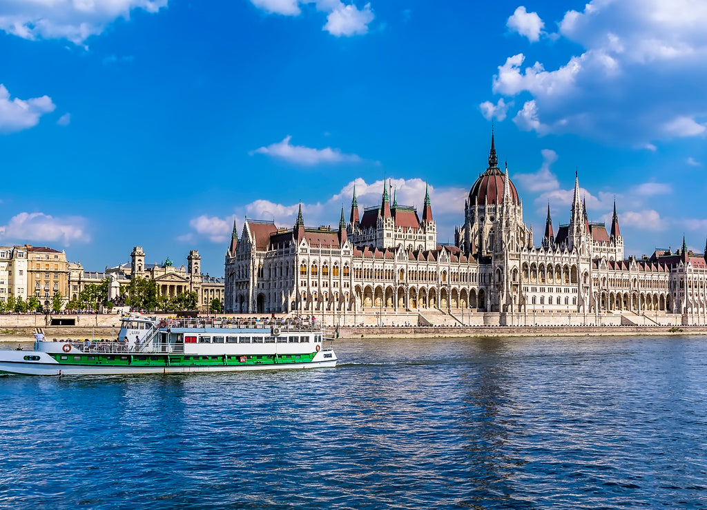 A ferry boat passes along the eastern shore of the River Danube in Budapest past the Parliament building in the summertime