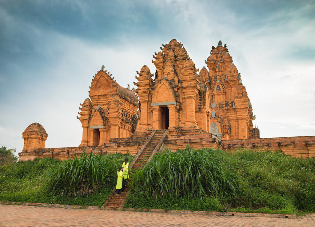 Champa temple - Hidu Tower in Asia. Vietnamese women in traditional dress Ao Dai walking toward the temple