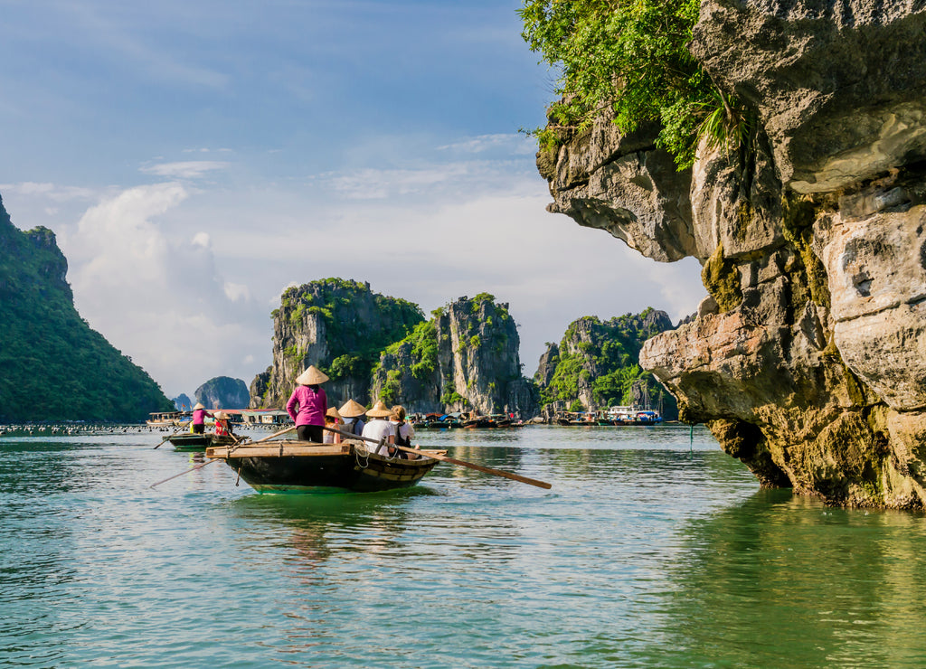 Tourists enjoying a boat trip with local guides through the majestic limestone mountains of Halong bay, Vietnam
