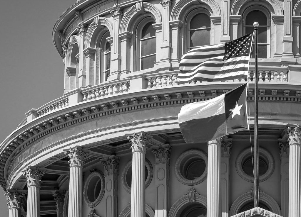 American and Texas state flags flying on the dome of the Texas State Capitol building in Austin in black white