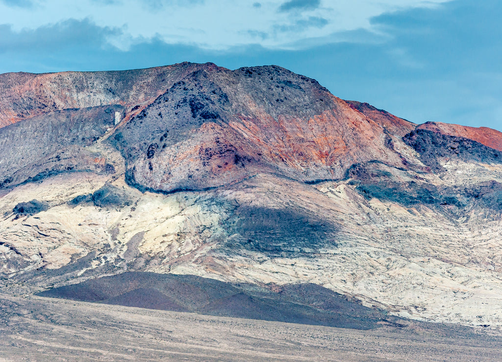 High Desert, Nevada, USA: Closeup of high mineral rich colored mountain and black hill under blue cloudscape