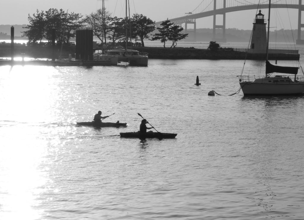 Two kayakers are out i the evening water, near the Newport Pell Bridge in Newport, Rhode Island in black white