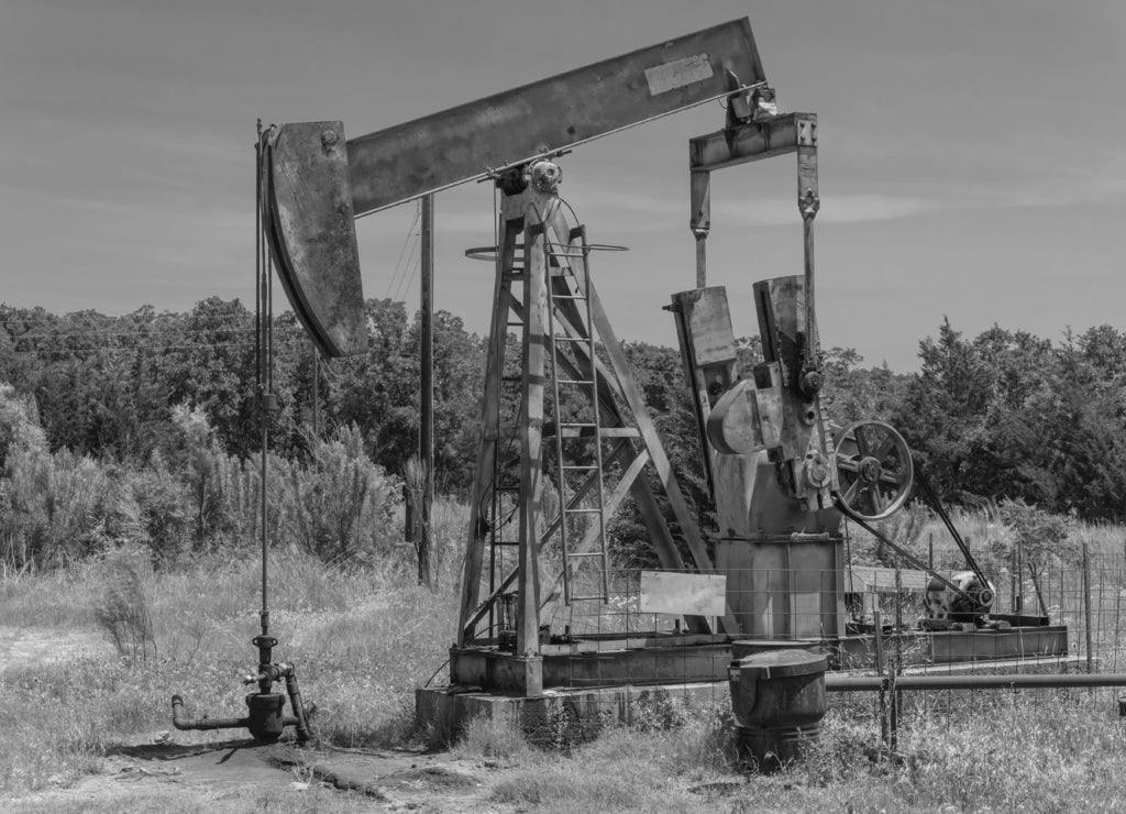 Close-up working pump jack fracking crude extraction machine. Pumping crude oil out of well to tank. Pumper, water emulsion at oil drilling site in Gainesville, Texas, US. Energy, Industrial background in black white