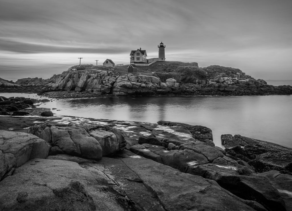 Colorful sunrise at Nubble Lighthouse, with dark rocks in the foreground and the rocky island hosting the lighthouse in the background in black white