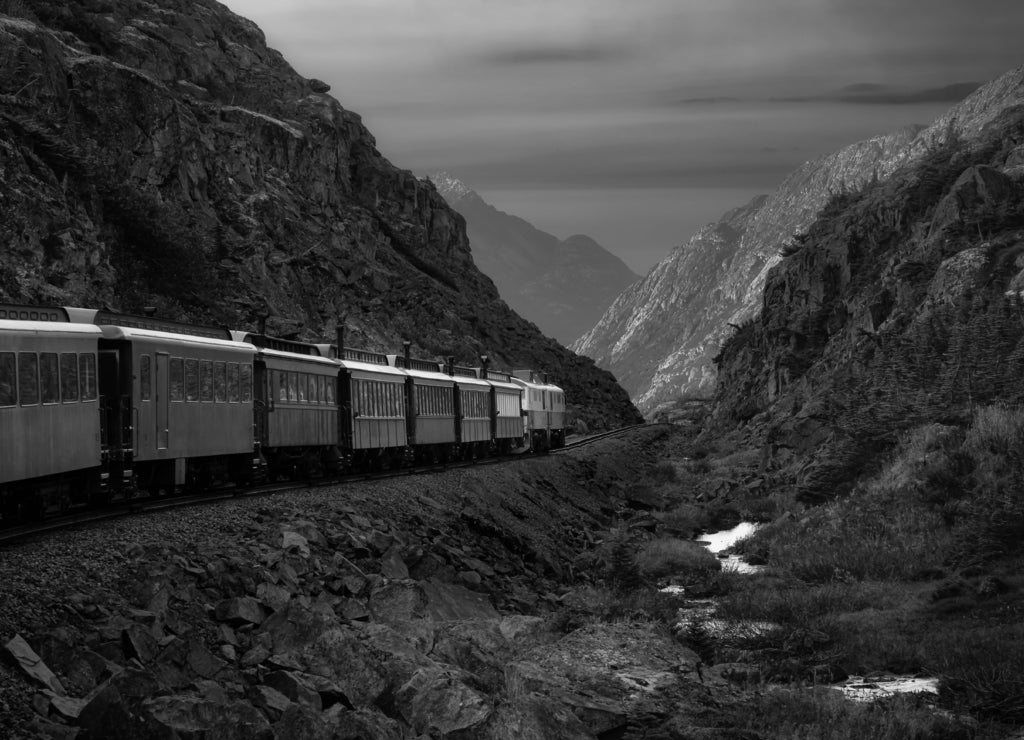 Old Historic Railroad Train is going over White Pass. Moody Colorful Sky Composite. Skagway, Alaska, United States in black white