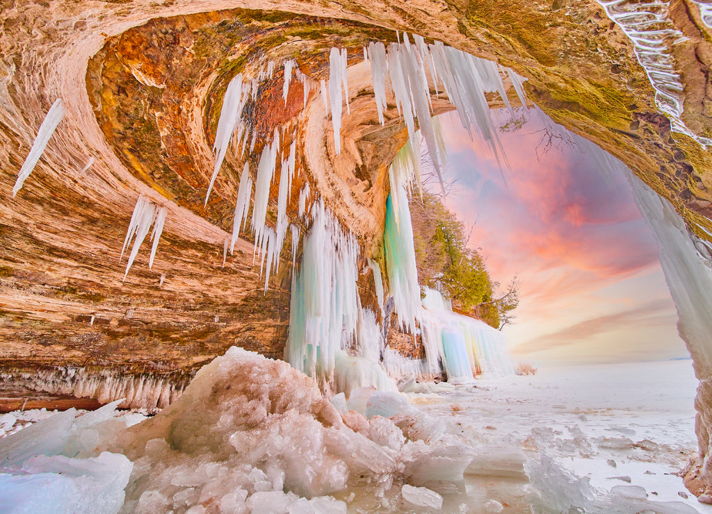 Ice cave entrance during sunrise on Lake Michigan with icicles and broken ice