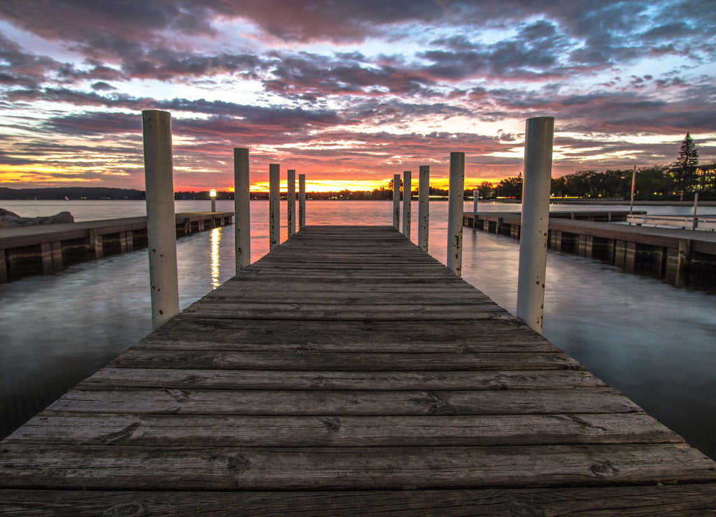 Wooden Dock On Sunrise Lake. Summer sunrise over the waters of Grand Traverse Bay in Traverse City, Michigan. Shot with long wooden dock in foreground sunrise over water at horizon